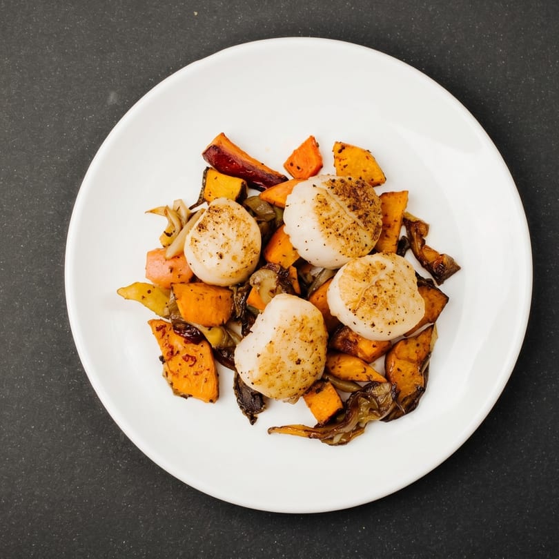Seared scallops with roasted butternut squash, carrots, and mushrooms on a white plate.