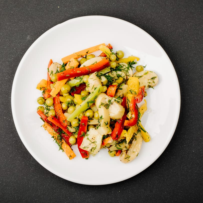 Colorful mixed vegetable salad with carrots, bell peppers, peas, and dill on a white plate.