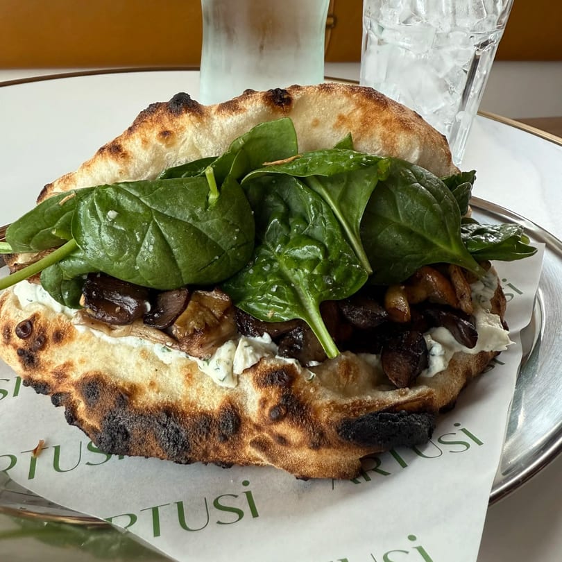 A calzone-like sandwich with spinach, mushrooms, and white sauce on Cartusi branded paper.